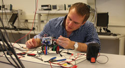 Male professor working on a lab bench, building a small robot with three wheels